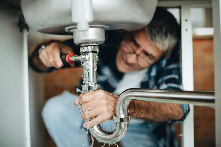 A person turning off the main water supply valve in a residential basement.