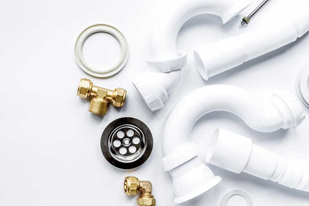 A person attaching a hose to the drain valve of a standard home water heater in a garage or utility room.