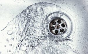 A person removing hair and debris from a bathroom sink drain stopper with their hands.
