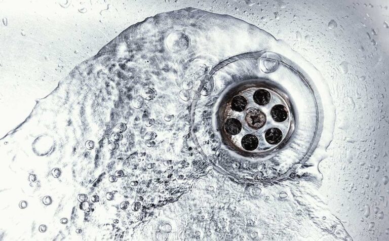 A person removing hair and debris from a bathroom sink drain stopper with their hands.