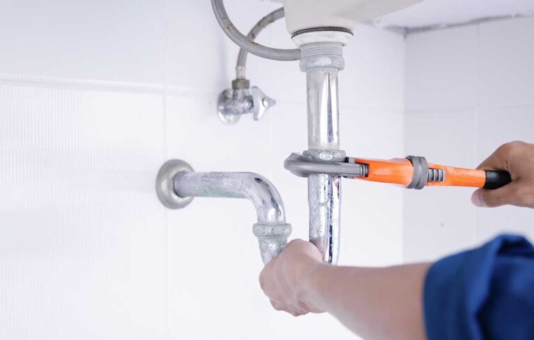 A person gently warming an exposed household pipe with a hair dryer in a home utility area.