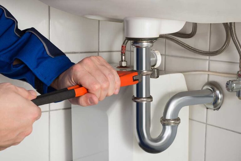 A damp basement with a floor drain, plumbing pipes, and a homeowner inspecting the source of a sewage odor.