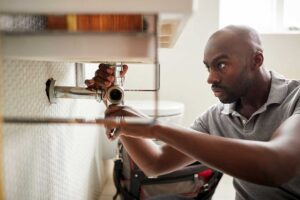 Hands replacing a rubber washer inside a wall-mounted outdoor faucet beside a garden hose.